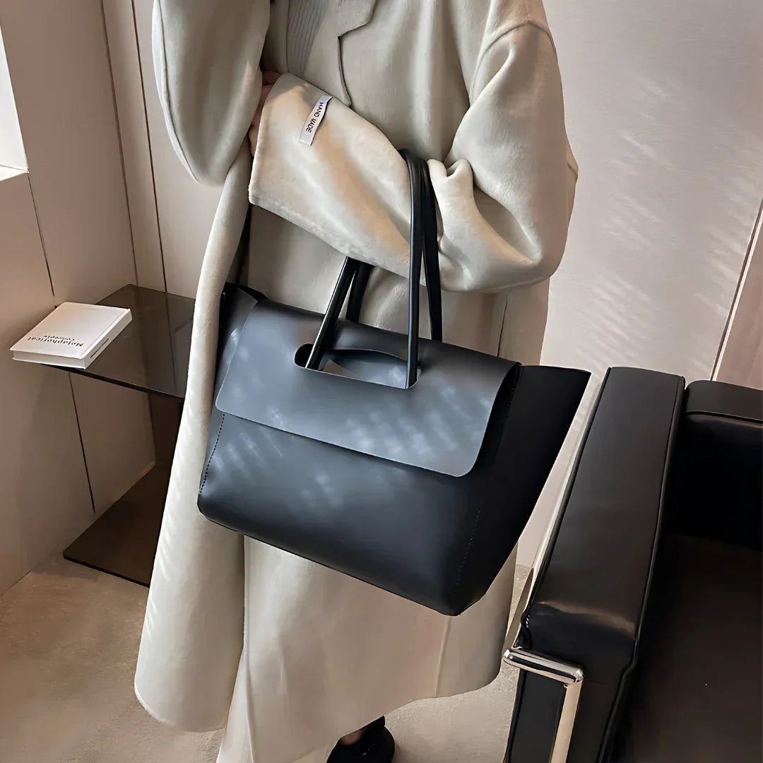 Woman in beige coat holding black leather tote bag in modern minimalist room