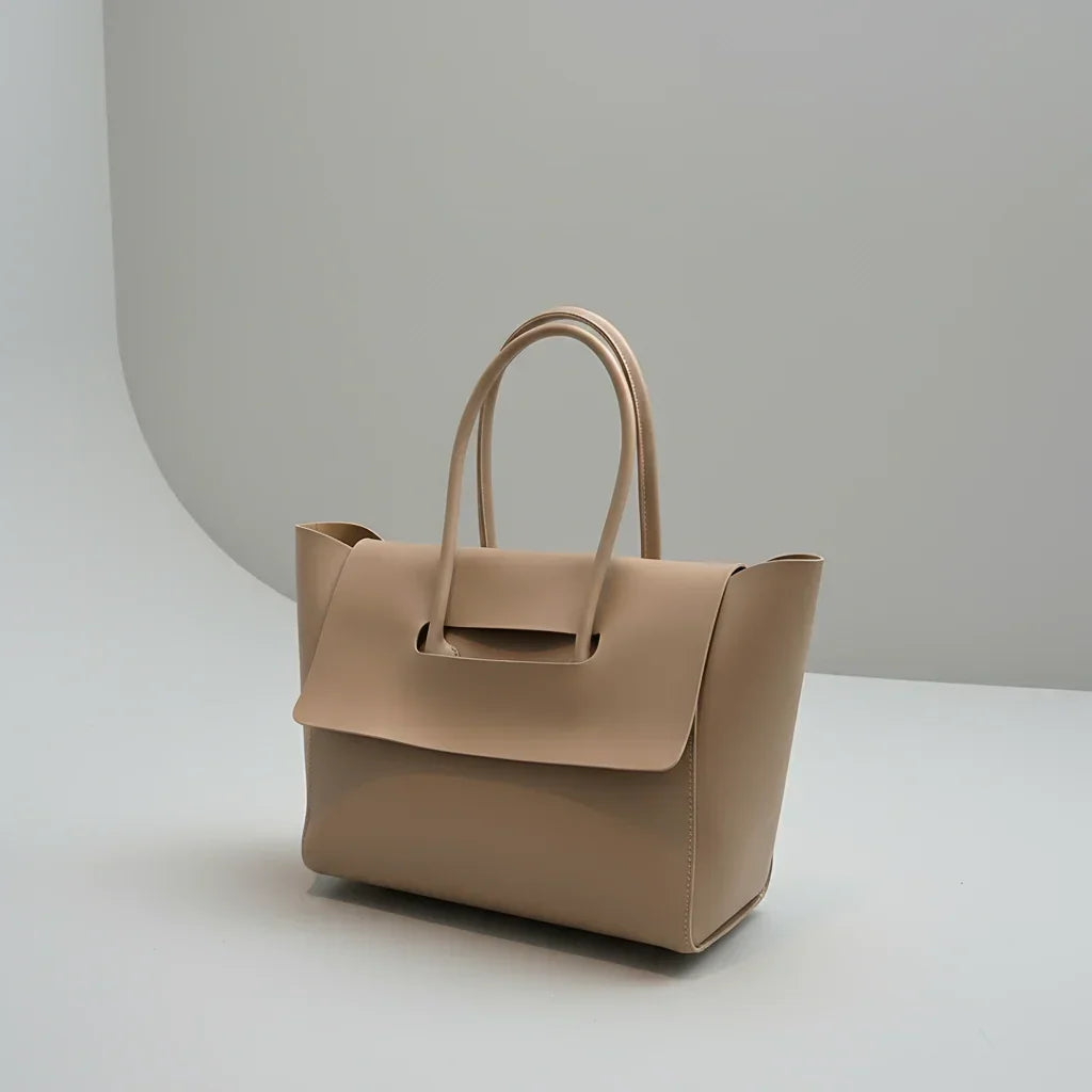 Beige leather tote handbag with top handles on a minimalist gray background
