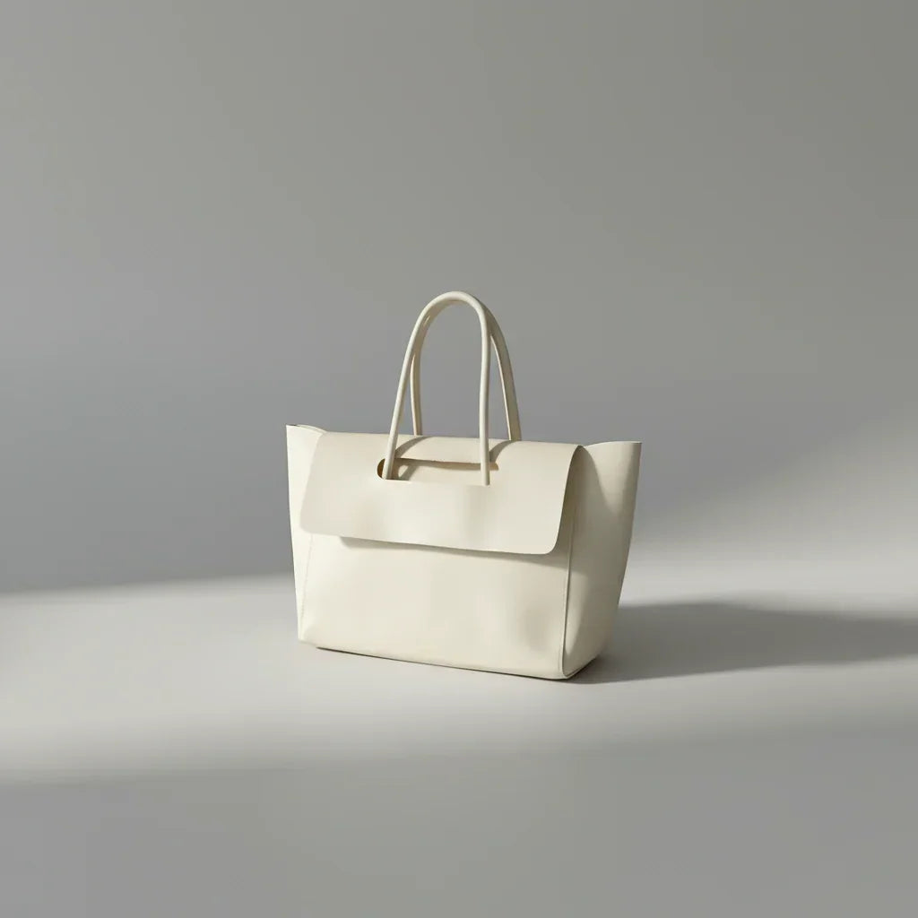 Minimalist cream leather tote bag with top handles on a light gray background