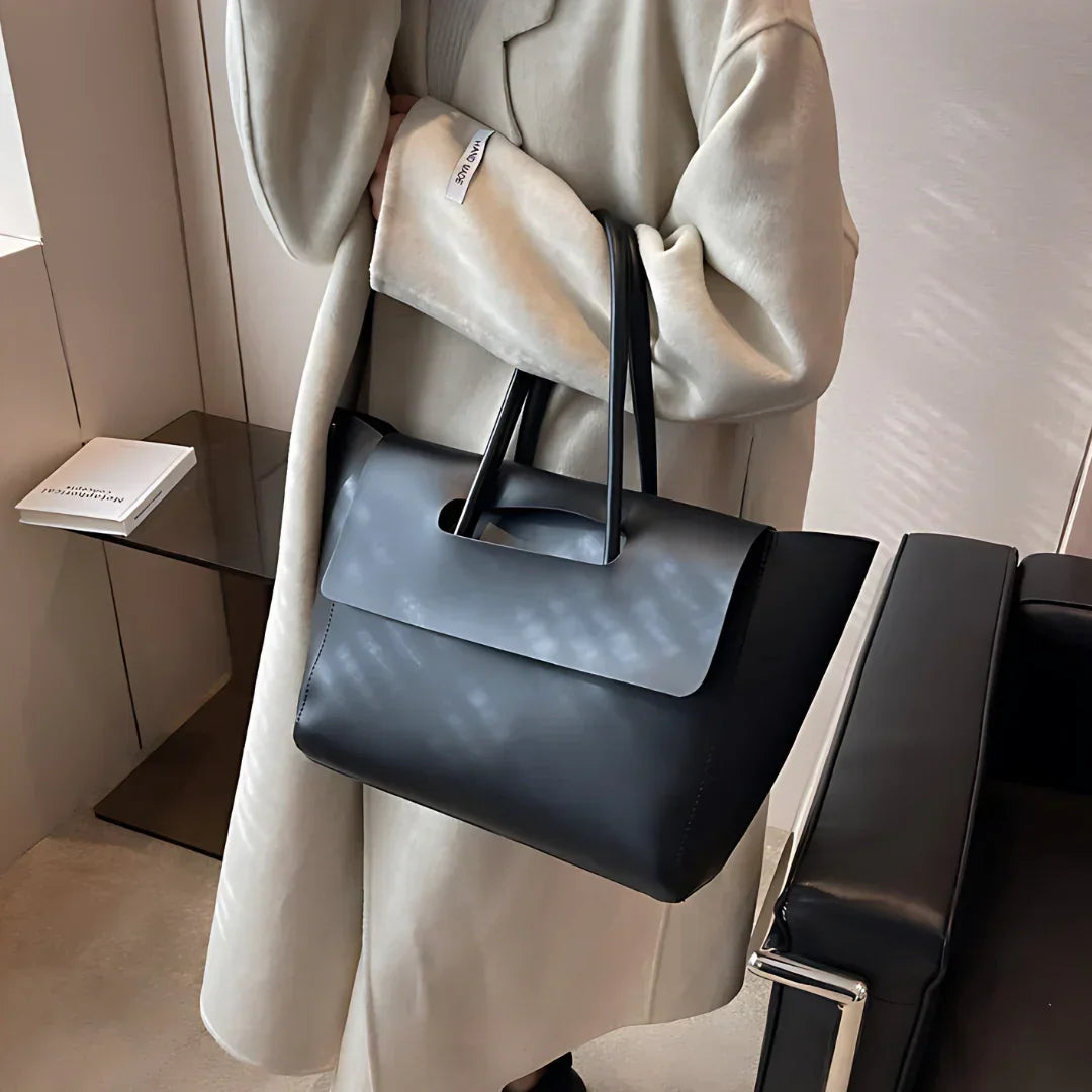Woman in beige coat holding large black leather tote bag in modern office setting