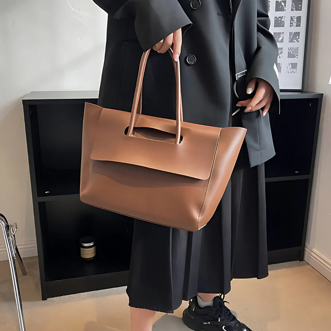 Woman in black outfit holding a large brown leather tote bag indoors