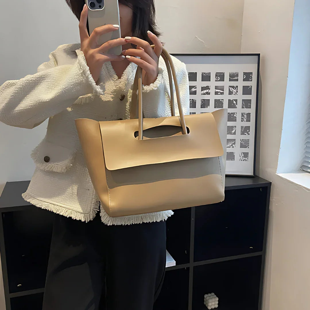 Woman in white jacket holding beige leather tote bag, taking mirror selfie indoors