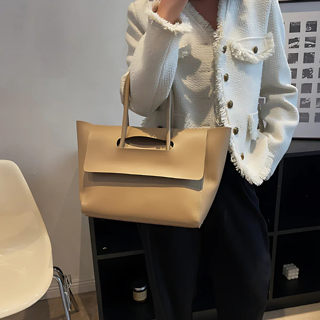 Woman in a white textured jacket holding a large beige leather tote bag indoors