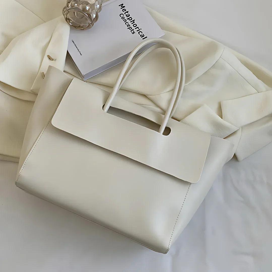 Minimalist white leather tote bag on cream blazer with book and decorative glass