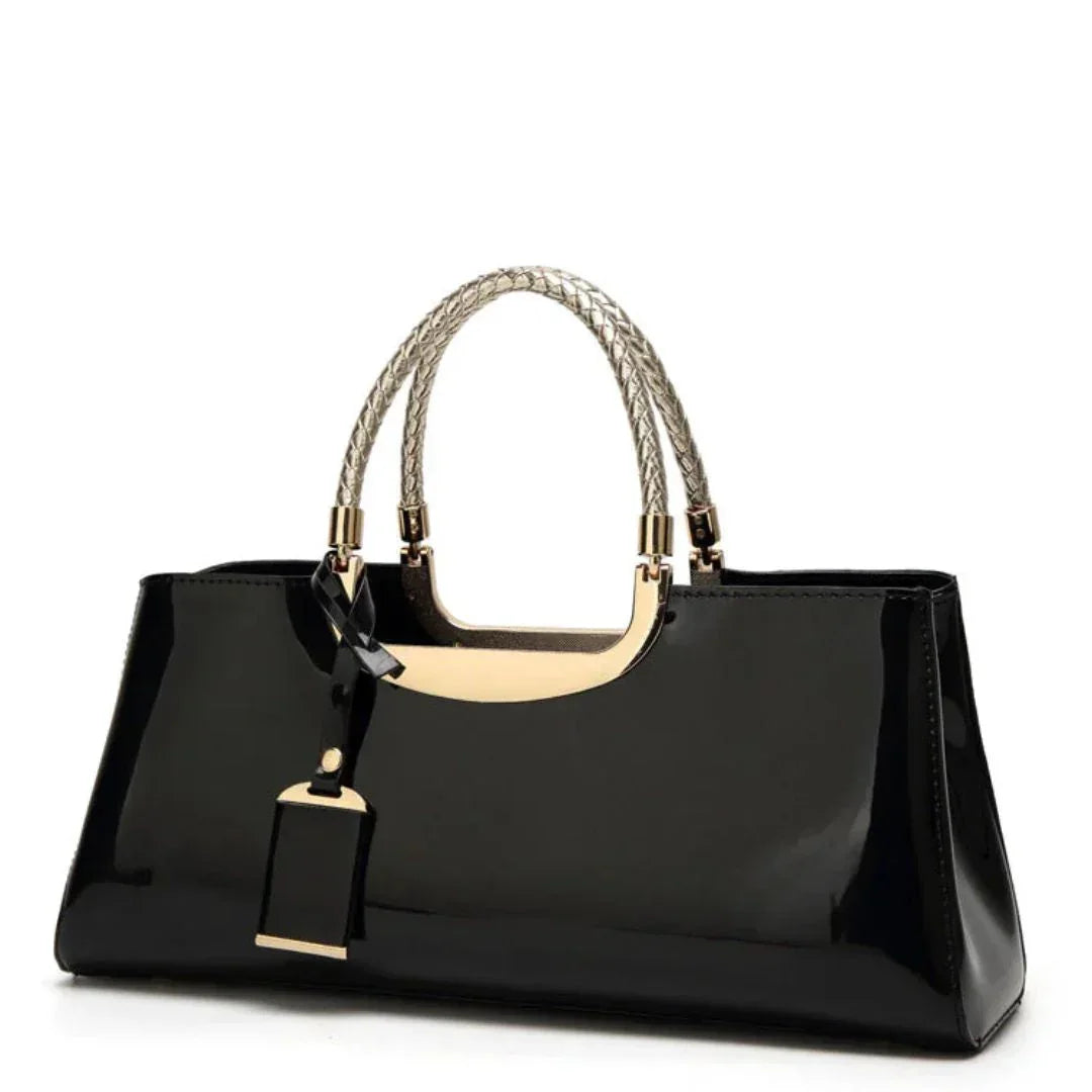 Glossy black handbag with gold handles and braided straps on white background