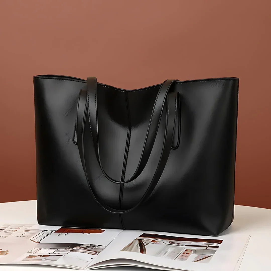 Black leather tote bag on white table with open magazine, brown background