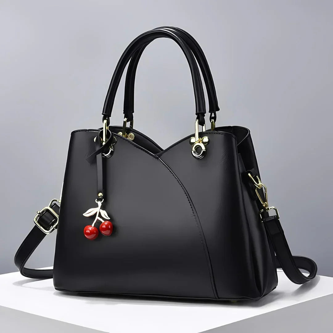 Black leather handbag with cherry charm and gold hardware on a white surface