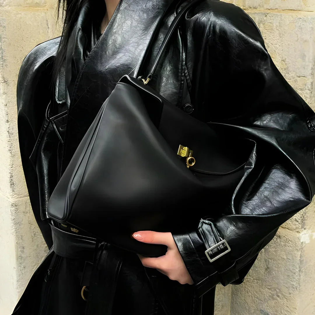 Woman in black leather coat holding a black leather handbag with gold hardware