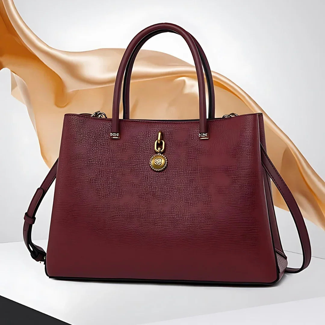 Elegant maroon leather handbag with gold charm on white and gold abstract background