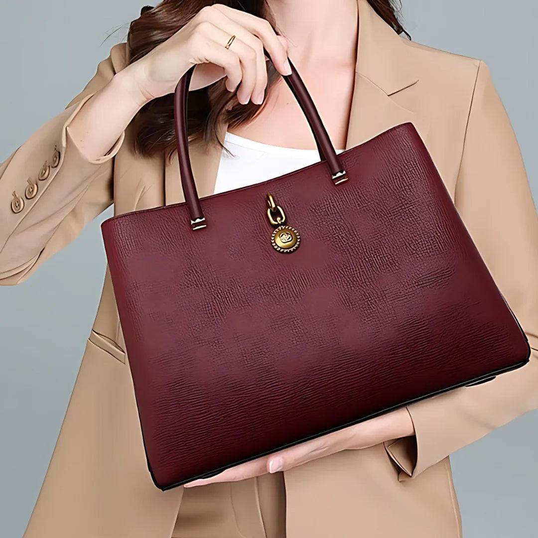 Woman holding a burgundy leather tote bag with gold hardware, beige blazer, fashion accessory