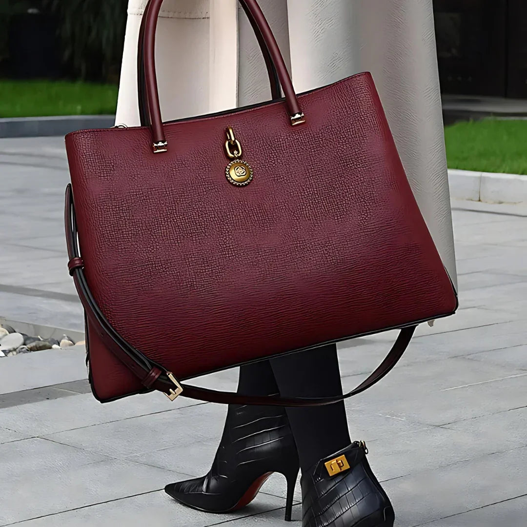 Woman holding large burgundy leather tote bag with gold hardware, wearing black heeled boots