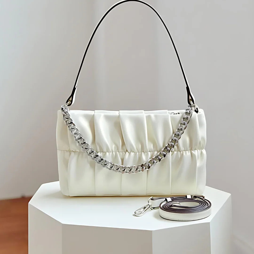 White ruched leather shoulder bag with silver chain and strap on white pedestal