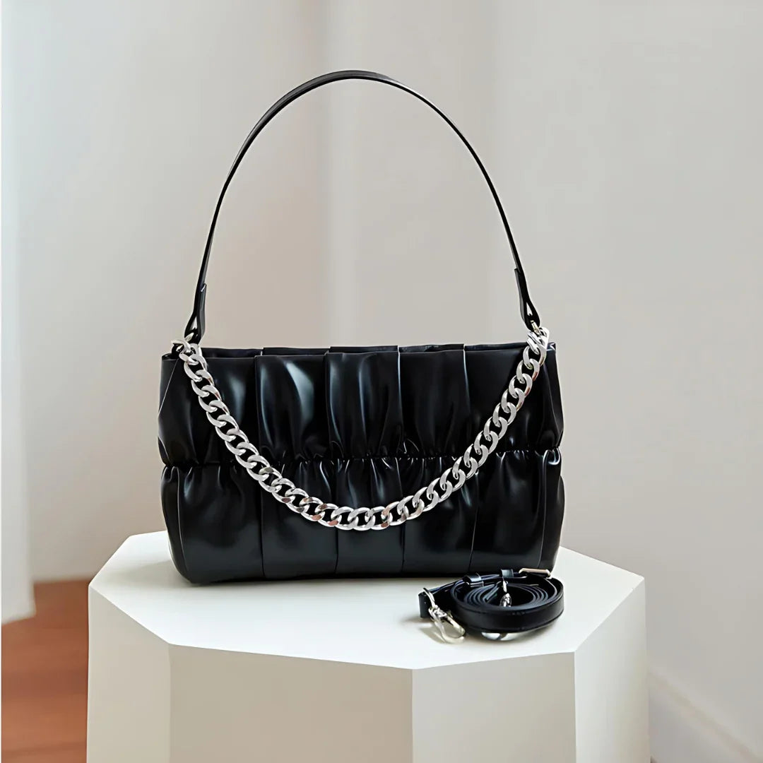 Black pleated handbag with chunky silver chain strap on white pedestal