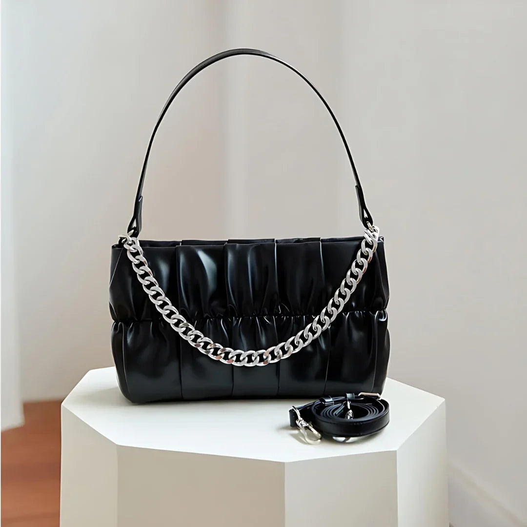 Black pleated handbag with chunky silver chain strap on white pedestal