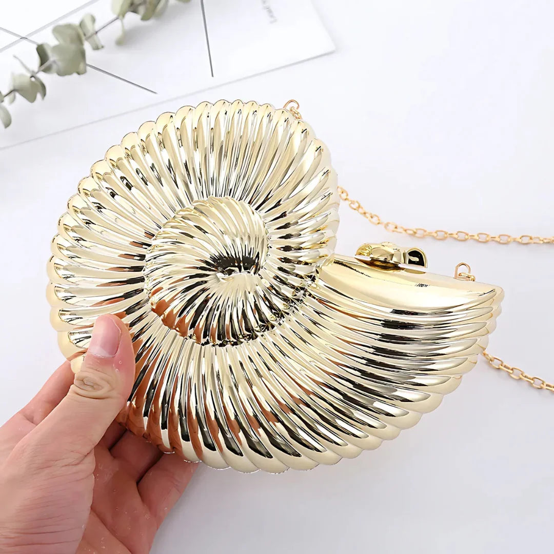 Gold seashell-shaped clutch handbag with chain strap held in hand on white background
