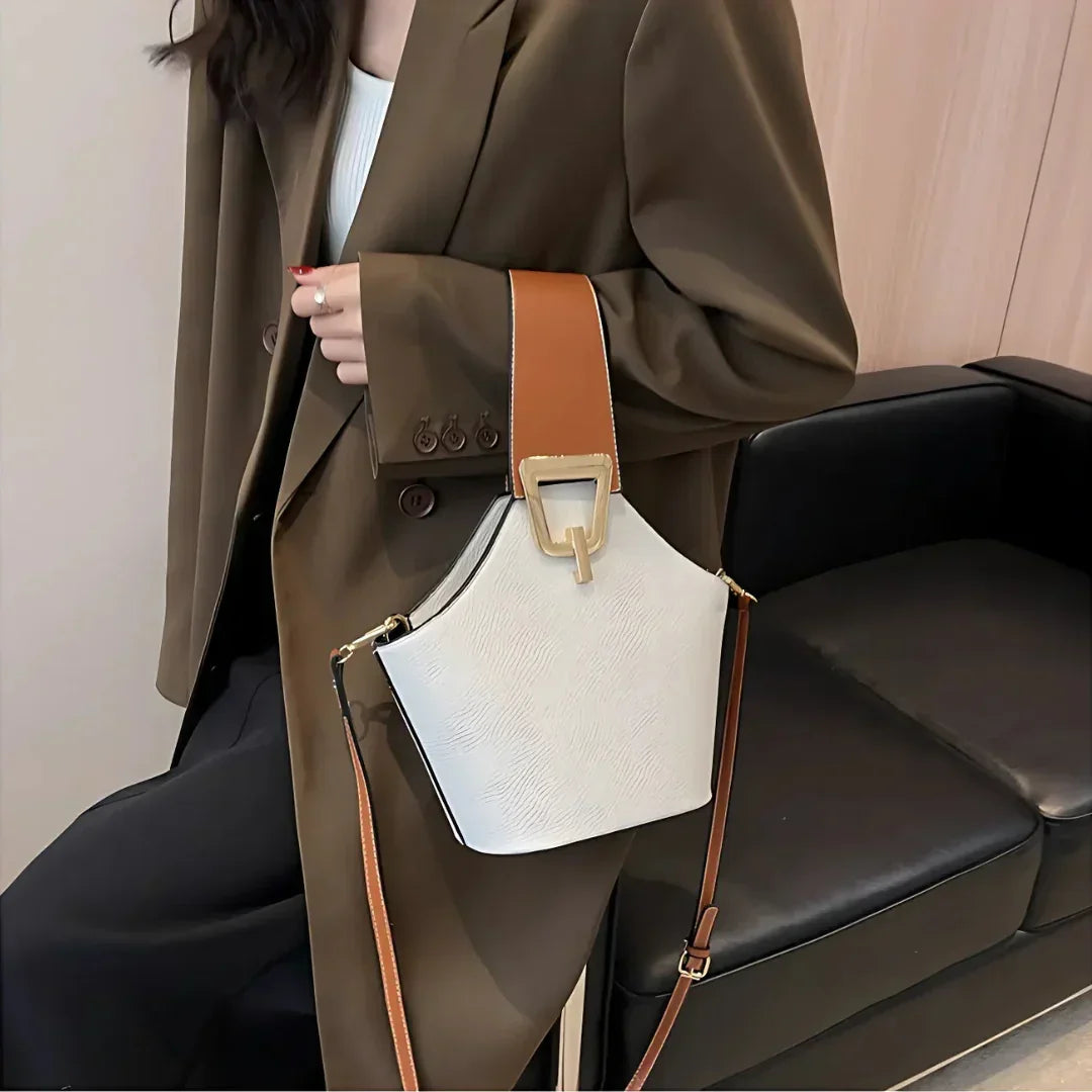 Woman in brown blazer with stylish white and tan leather handbag, modern interior background