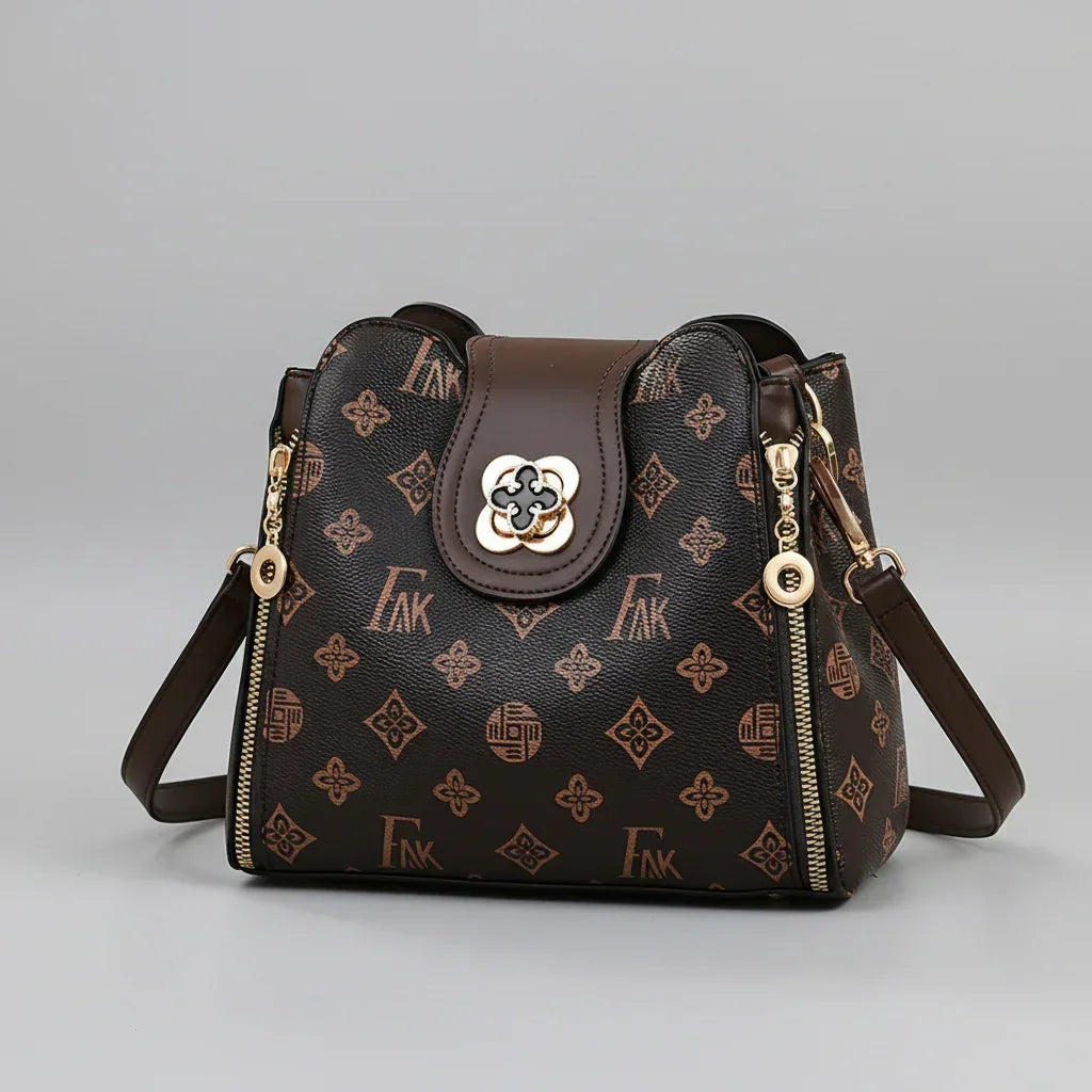 Brown patterned leather shoulder bag with gold accents and zipper details on gray background