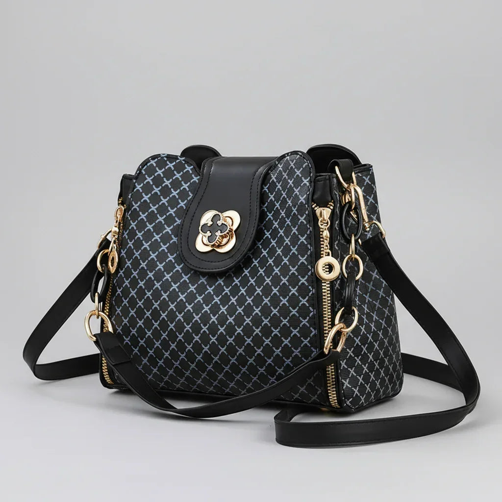Black designer handbag with gold hardware, geometric pattern, and adjustable strap on gray background