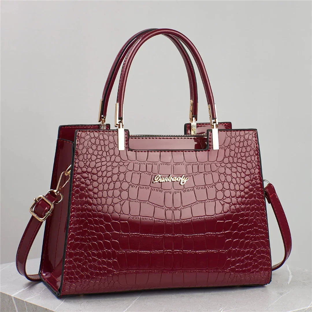 Glossy burgundy crocodile embossed handbag with gold hardware and dual top handles