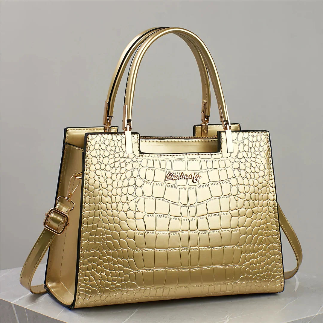 Gold crocodile-embossed handbag with top handles and shoulder strap on marble surface