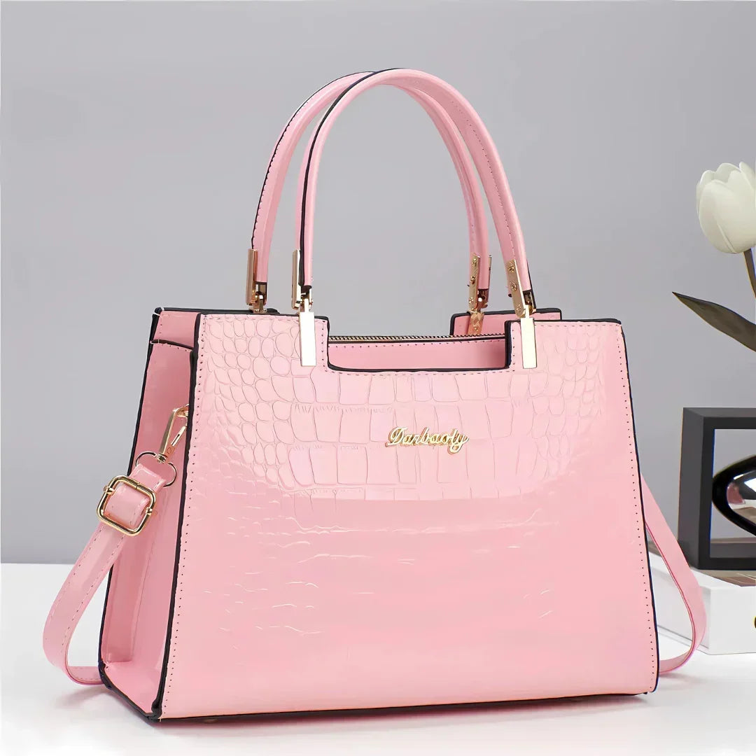 Pink crocodile-pattern faux leather handbag with gold hardware on white table