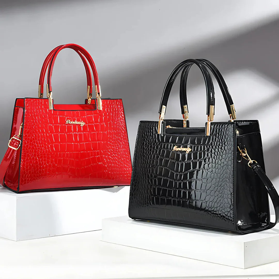 Red and black crocodile pattern handbags with gold handles on white display blocks