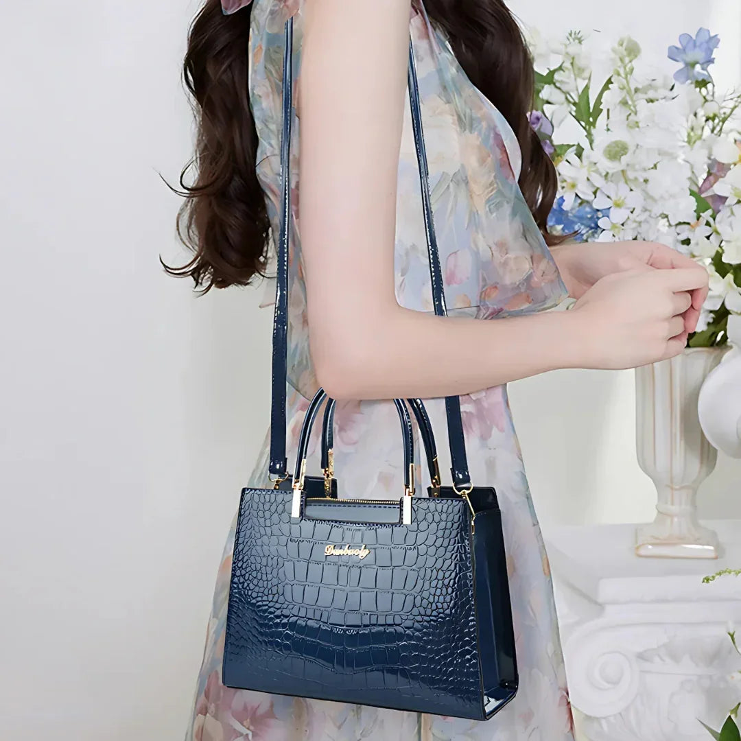 Woman in floral dress holding a navy blue crocodile pattern handbag with gold hardware
