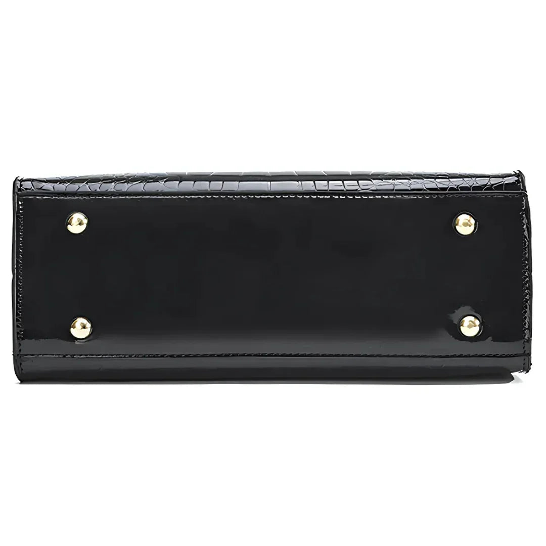 Bottom view of black patent leather handbag with gold metal feet and crocodile texture