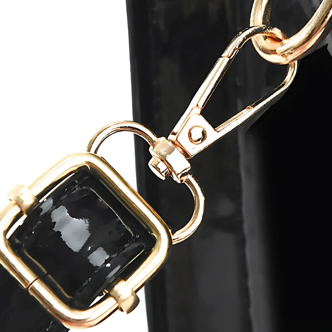Gold buckle and clasp on black patent leather handbag strap close-up