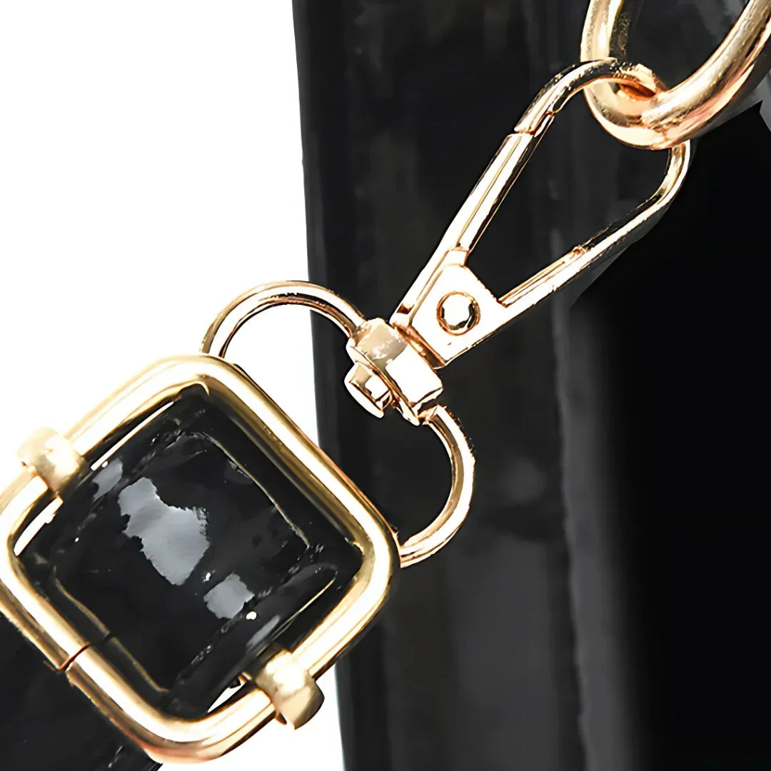 Gold buckle and clasp on black patent leather handbag strap close-up