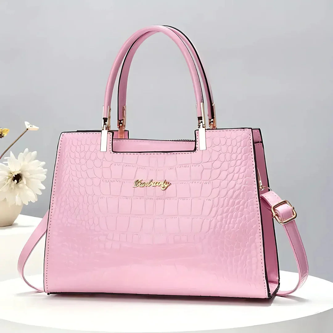 Pink crocodile pattern handbag with gold accents on a white table, flower decor
