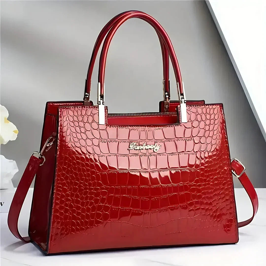 Glossy red crocodile-pattern handbag with gold hardware on white surface