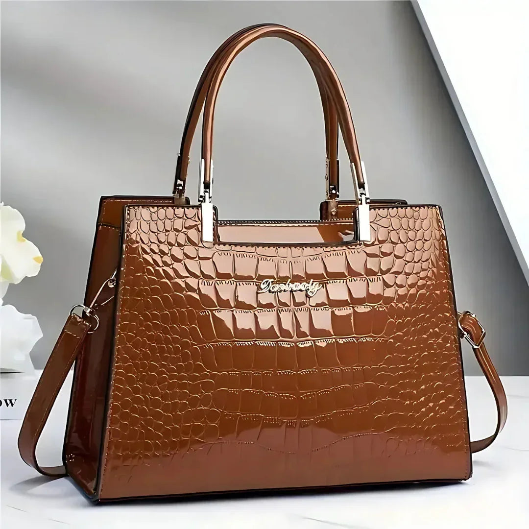 Glossy brown crocodile pattern leather handbag with double handles on a white table