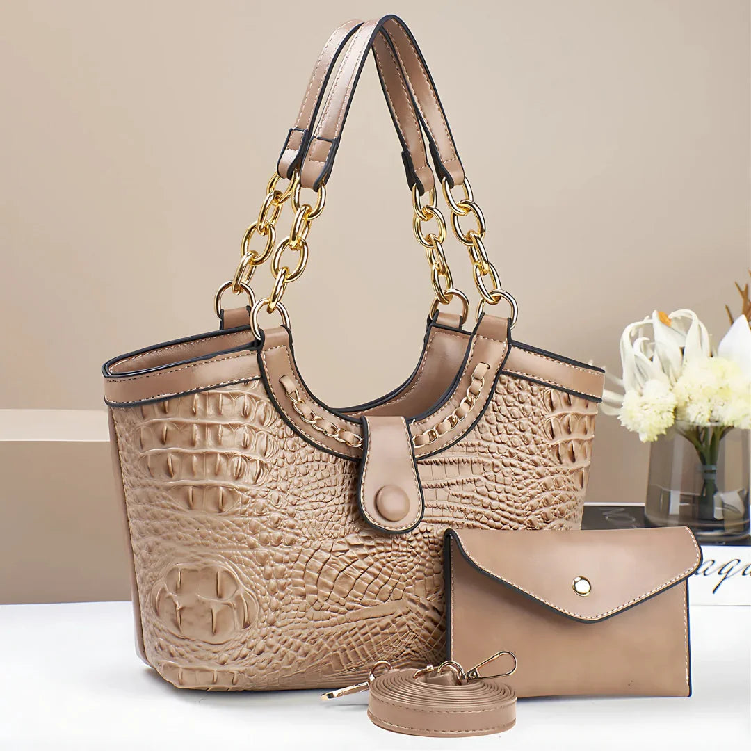 Beige crocodile-embossed handbag with gold chain straps, matching wallet, and strap on table