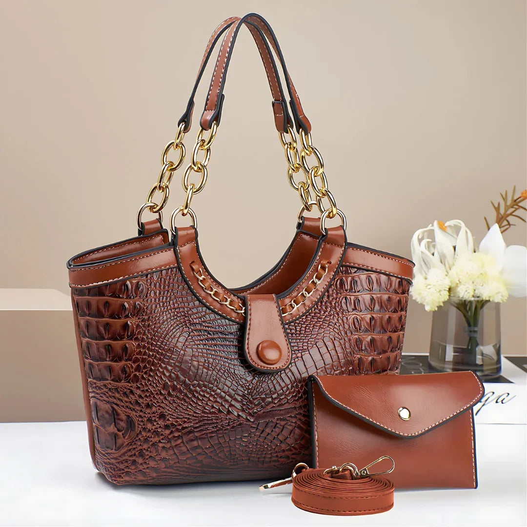 Brown crocodile pattern handbag set with gold chain handles and matching wallet on a white table