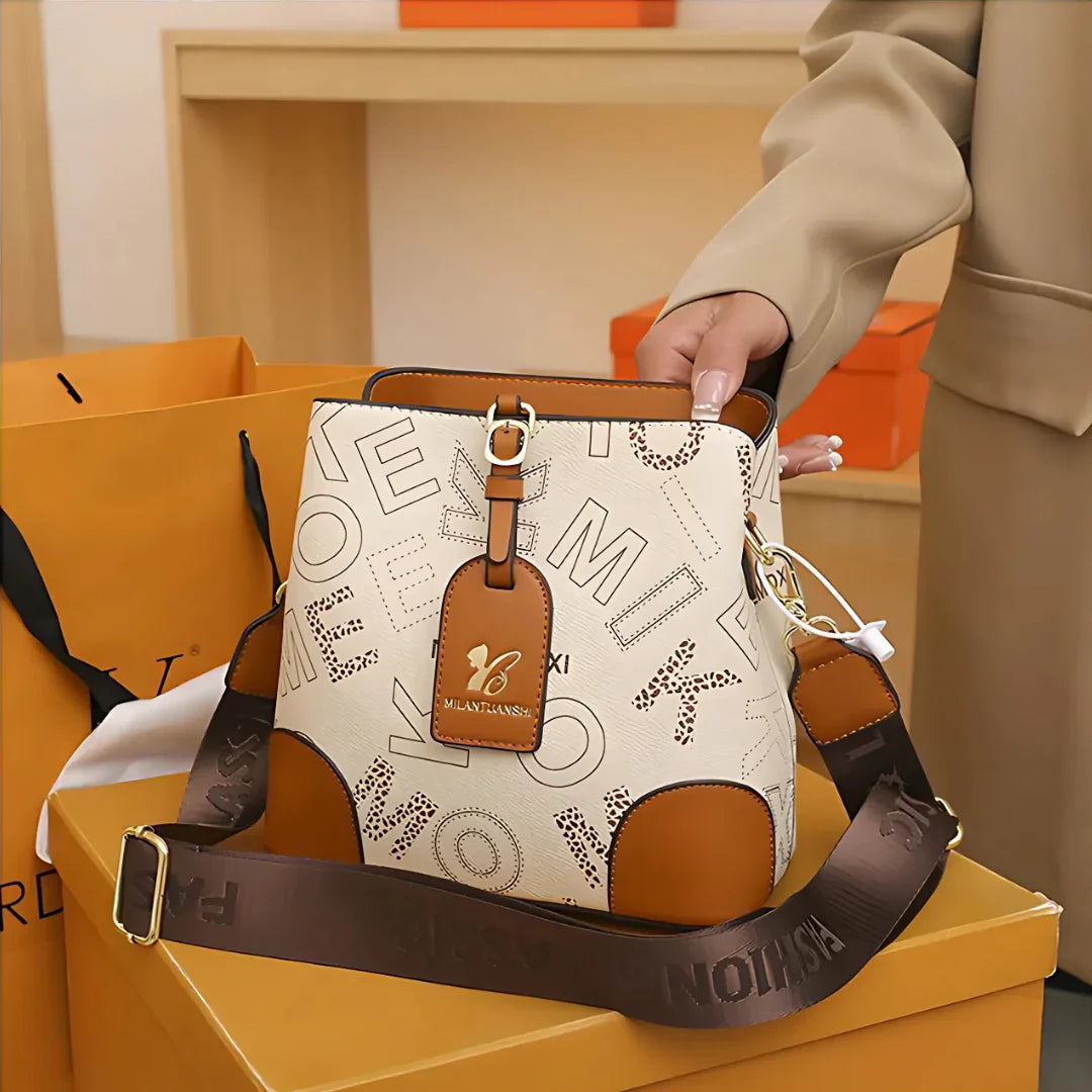 Beige and brown MILANTANXXI bucket bag with printed letters, held by person in beige coat