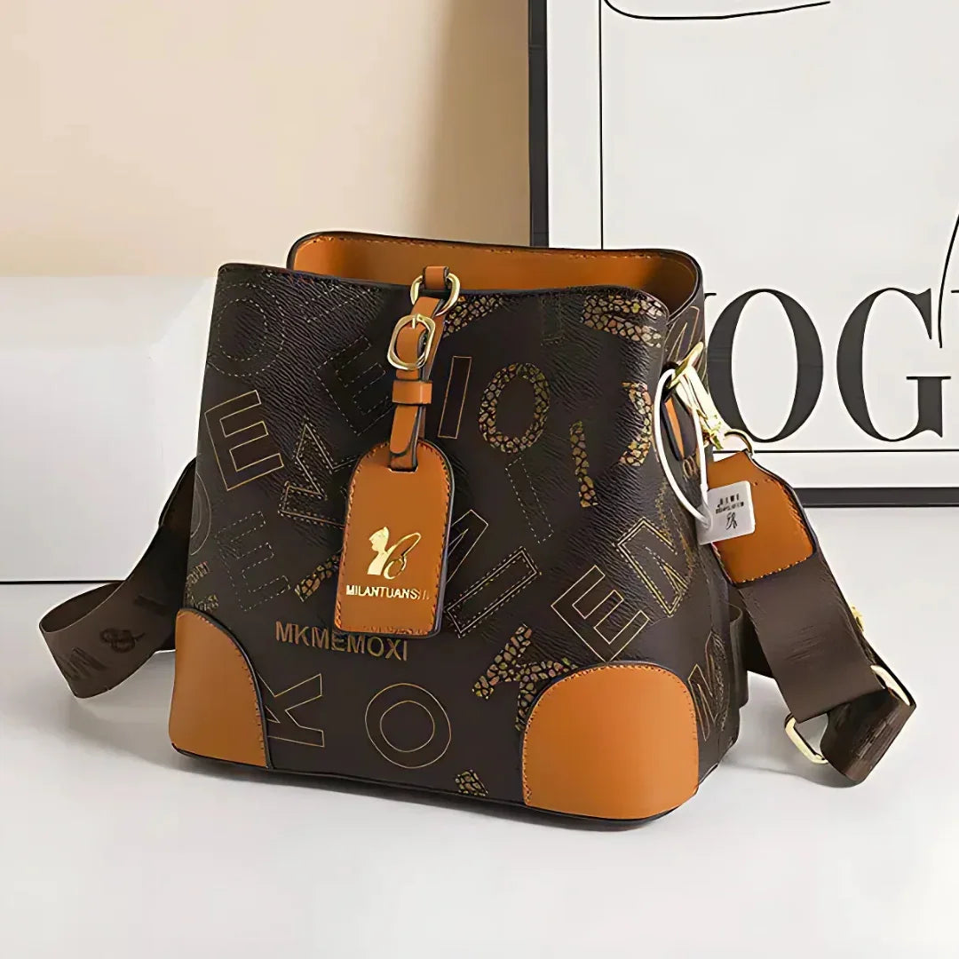 Brown and tan bucket bag with gold hardware and bold letter print, on white background