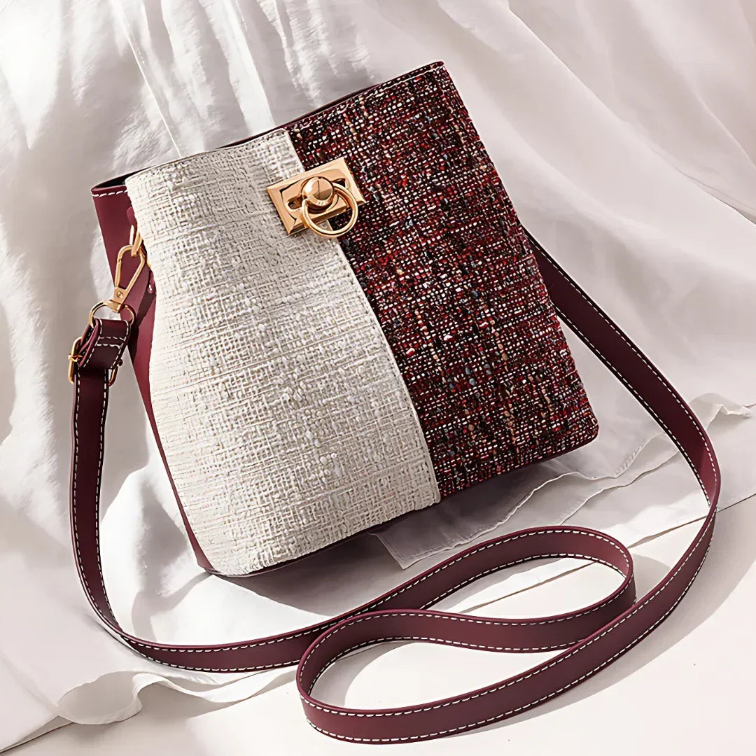 Two-tone textured bucket bag with gold clasp and burgundy strap on white fabric