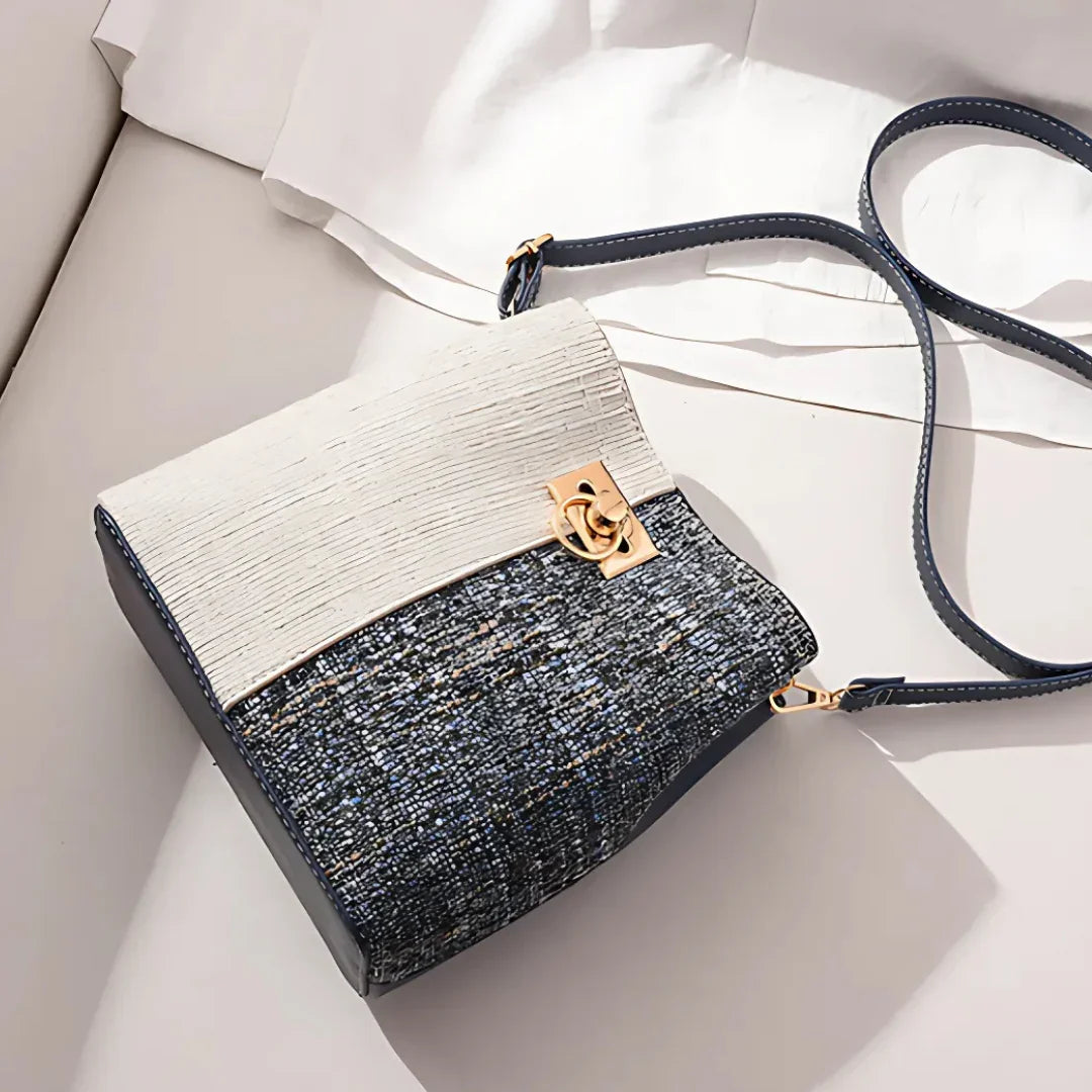 Elegant two-tone textured crossbody bag with gold clasp on a white fabric background