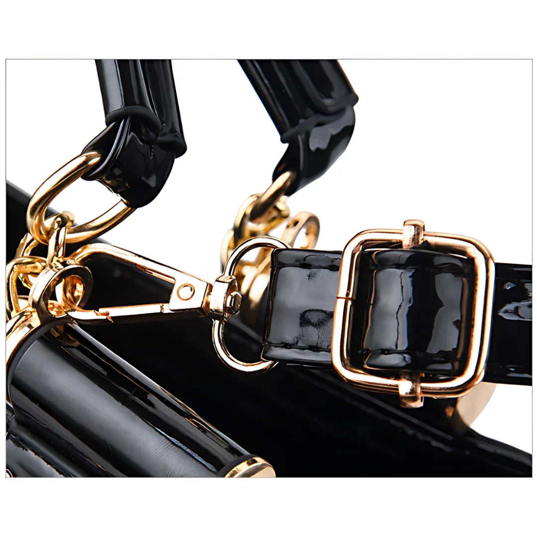 Close-up of a black patent leather handbag strap with gold buckle and hardware