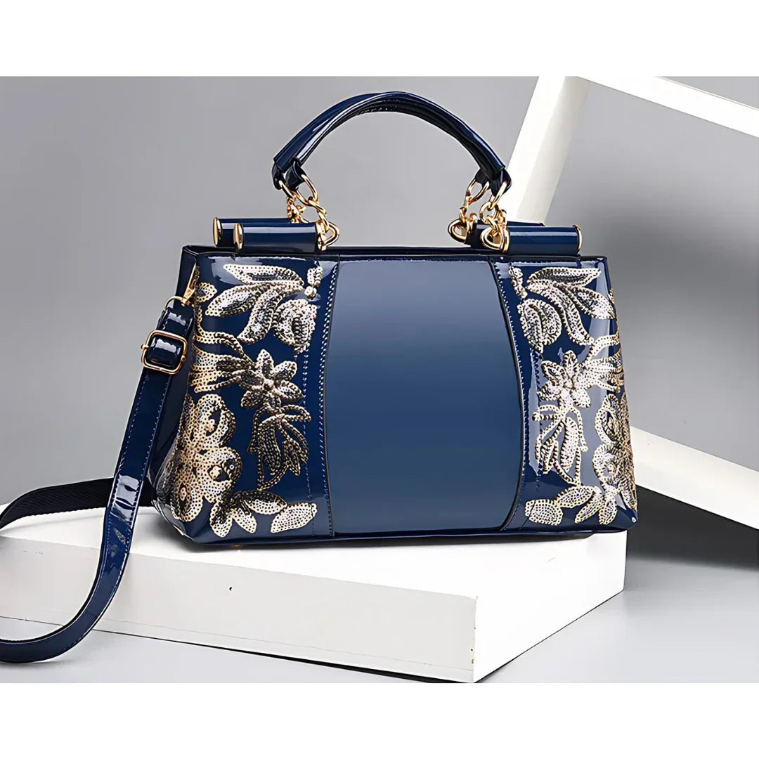 Blue patent leather handbag with gold floral sequins on white display stands