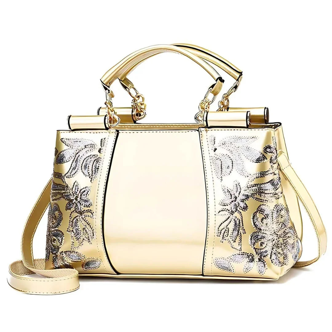 Gold handbag with floral patterns, top handles, and shoulder strap on white background