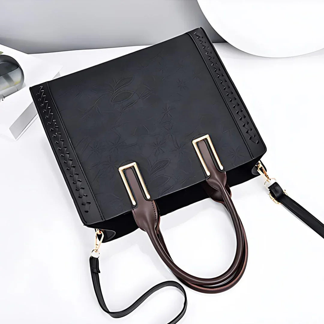 Black embossed leather handbag with gold accents and detachable strap on white background
