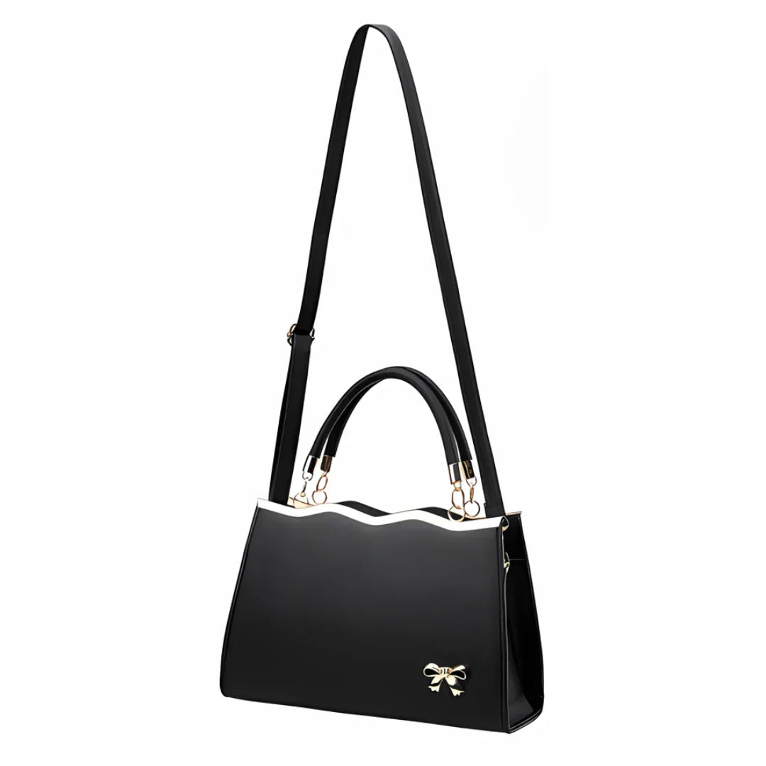 Black handbag with gold bow accent, wavy top edge, and adjustable shoulder strap