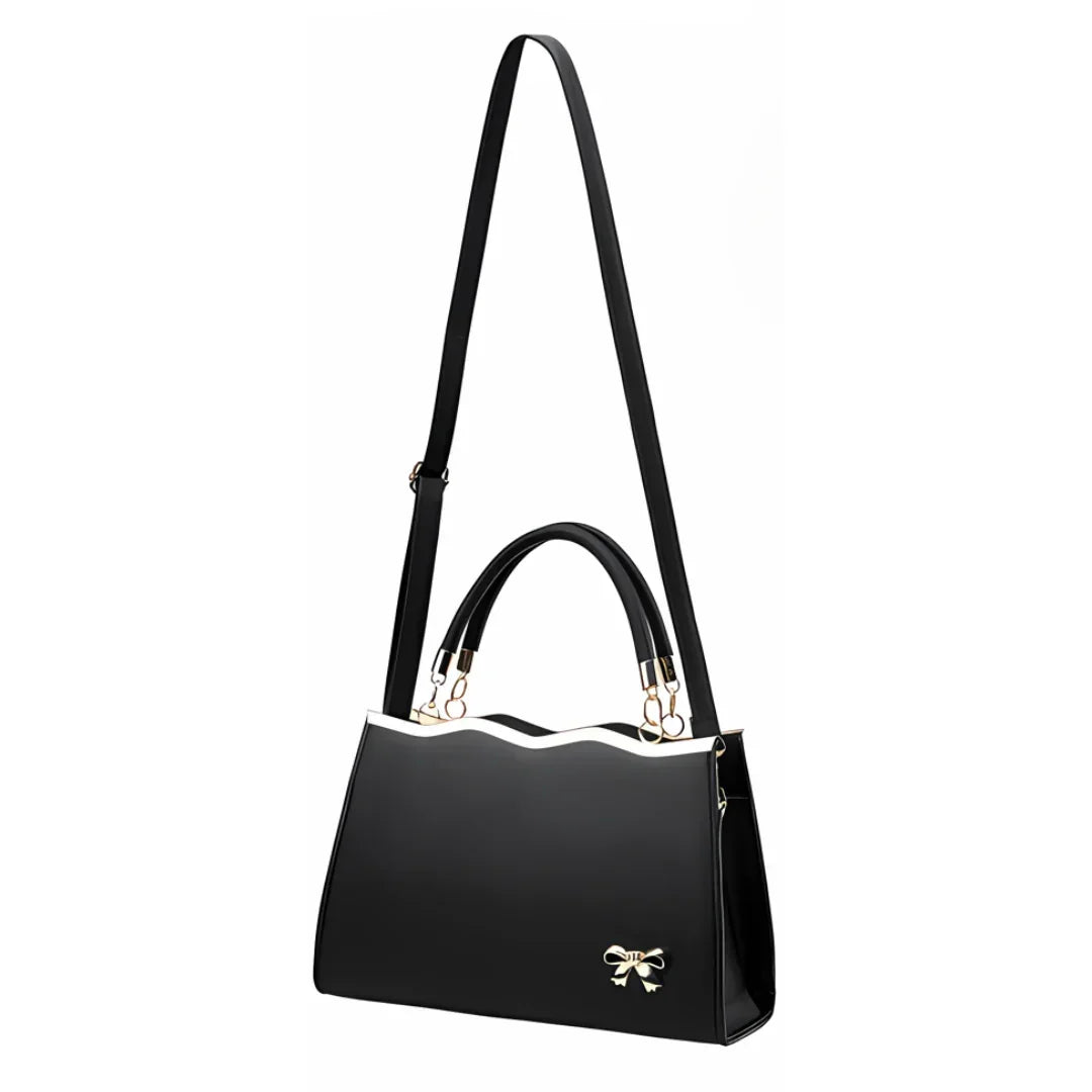 Black handbag with gold bow accent, wavy top edge, and adjustable shoulder strap