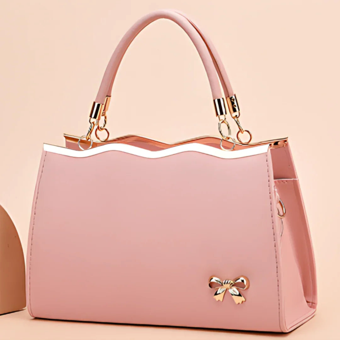 Elegant pink handbag with a gold bow charm and wavy top edge on a pastel background