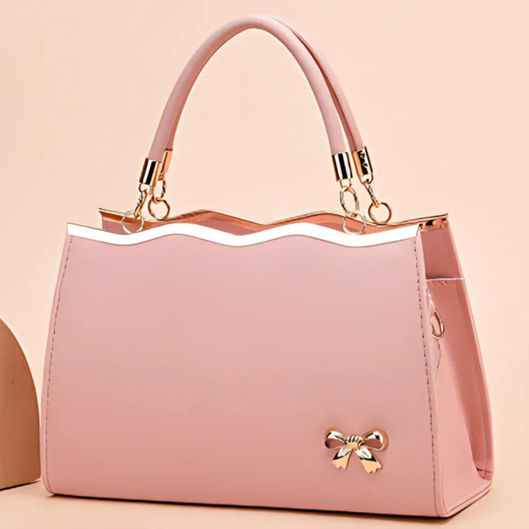 Elegant pink handbag with a gold bow charm and wavy top edge on a pastel background