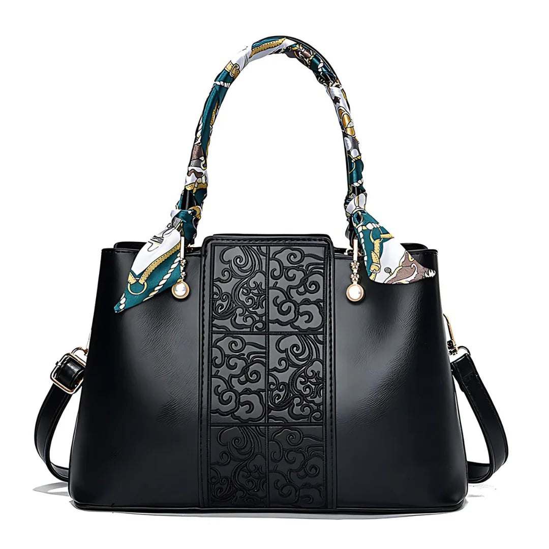 Black leather handbag with embossed floral pattern, printed scarf handles, and gold accents