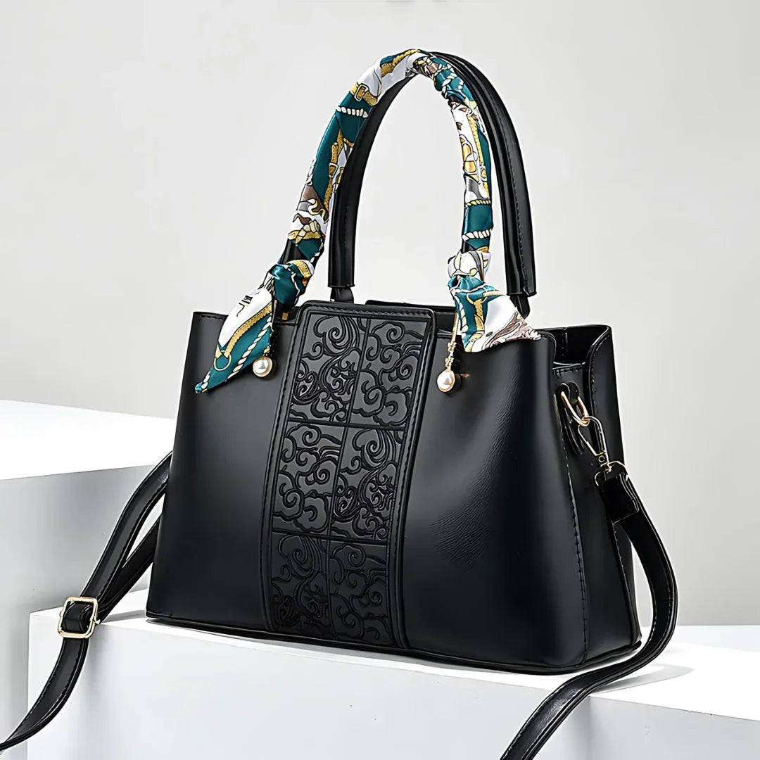 Black leather handbag with embossed front panel, patterned handle scarf, and gold hardware