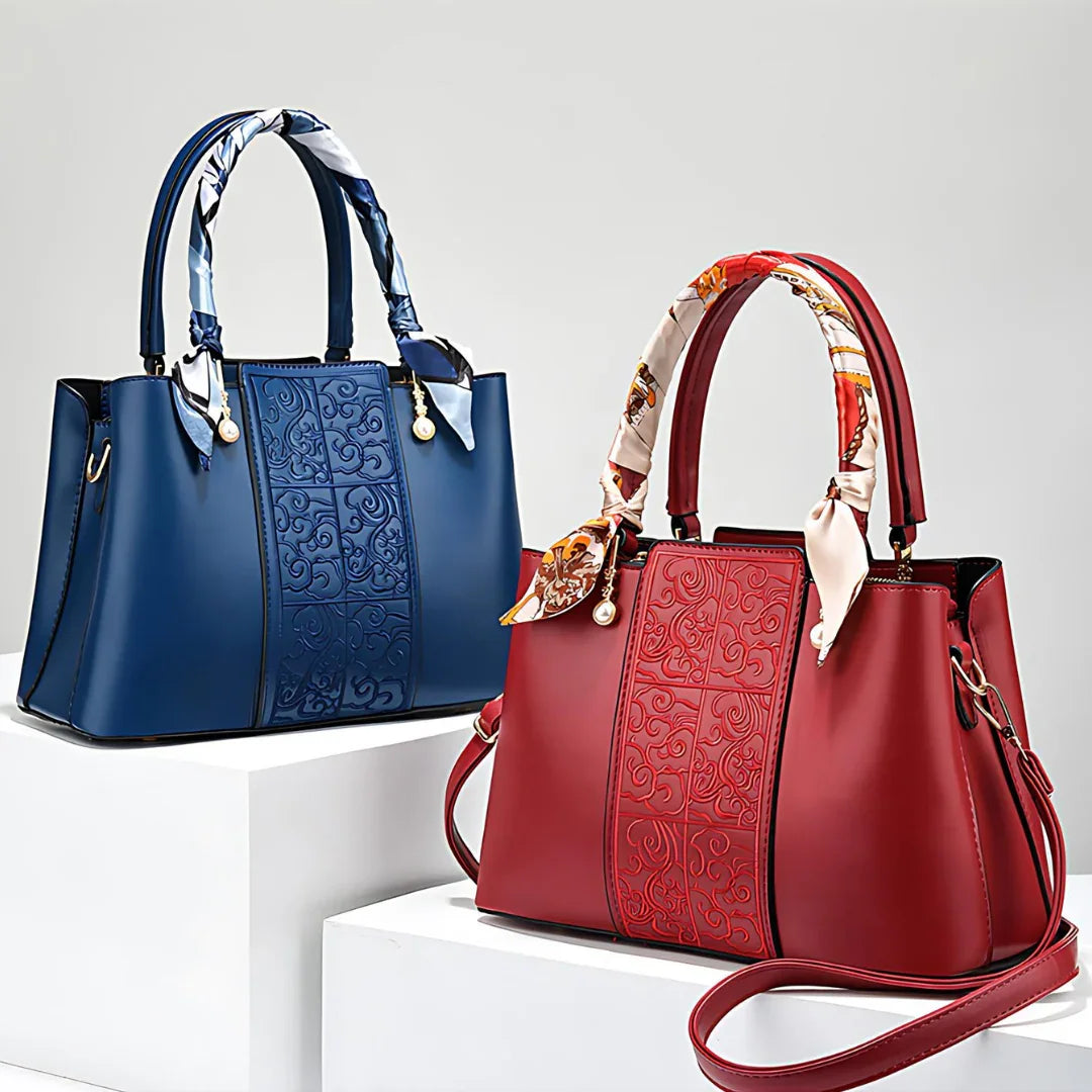 Blue and red embossed leather handbags with scarf handles on white display blocks